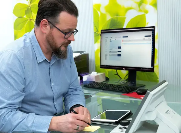 Mann arbeitet im modernen Büro am Computer, macht Notizen und nutzt digitale Geräte.