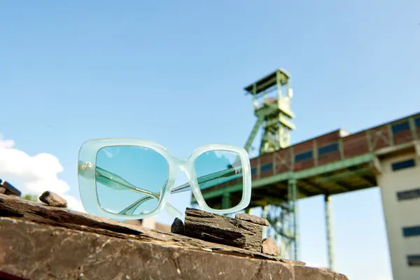 Stylische Sonnenbrille mit hellblauen Gläsern vor Industriegebäude bei Sonnenschein.